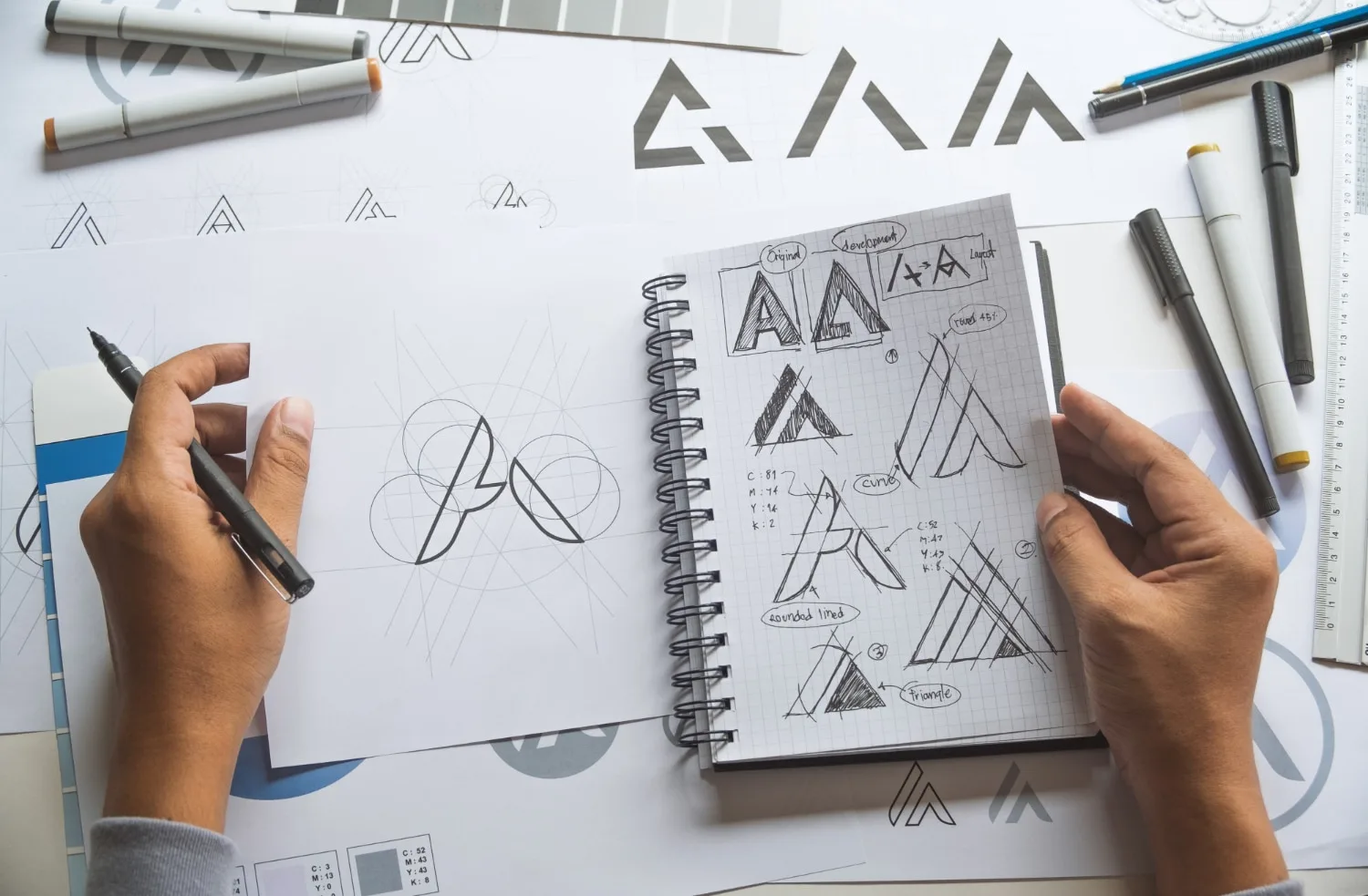 Graphiste travaillant sur la création d’un logo d’entreprise sur ordinateur avec esquisses, palette de couleurs et fichiers vectoriels.