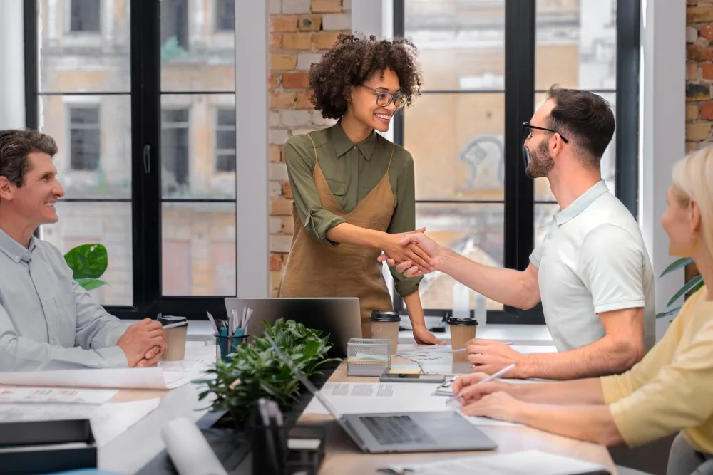 Deux entrepreneurs discutent devant un tableau affichant un projet à impact social, avec des graphiques de performance et des pictogrammes de solidarité