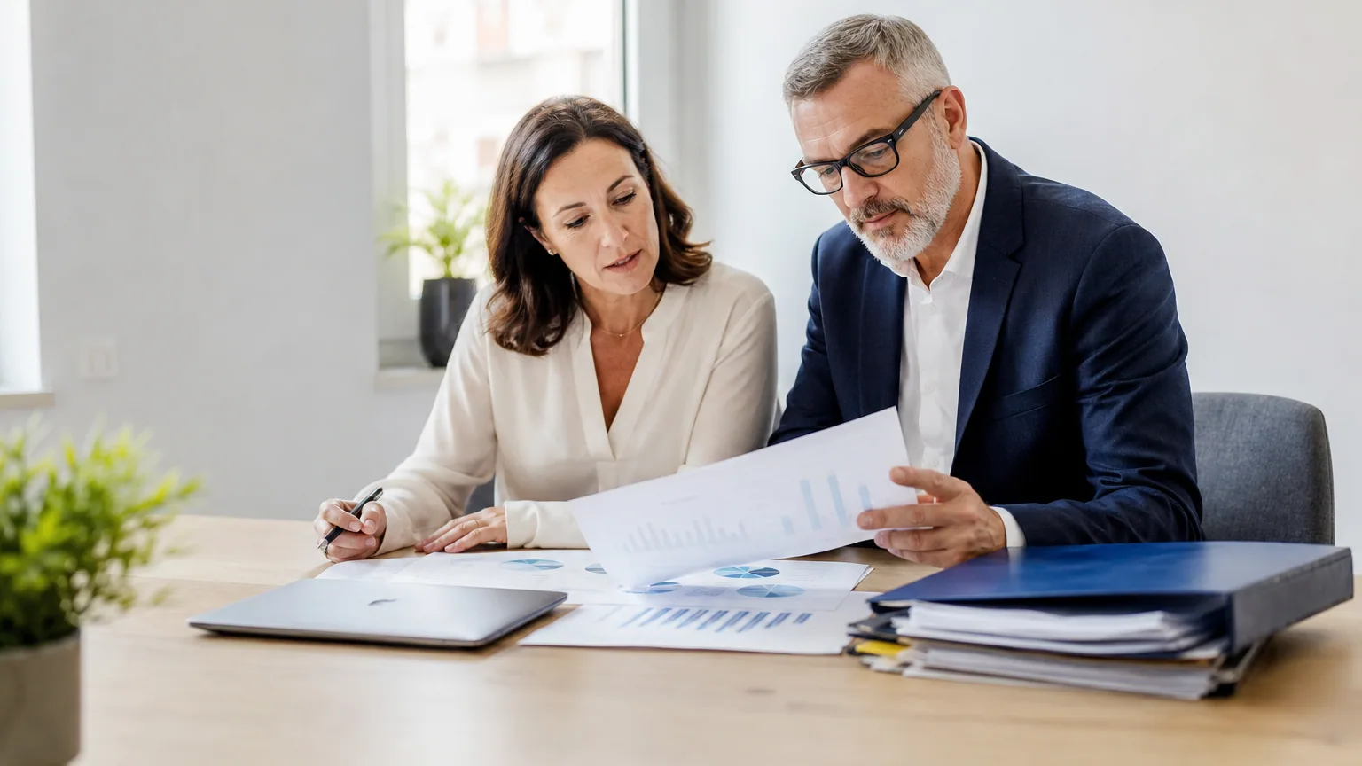 Deux professionnels analysent des documents financiers dans un petit bureau.