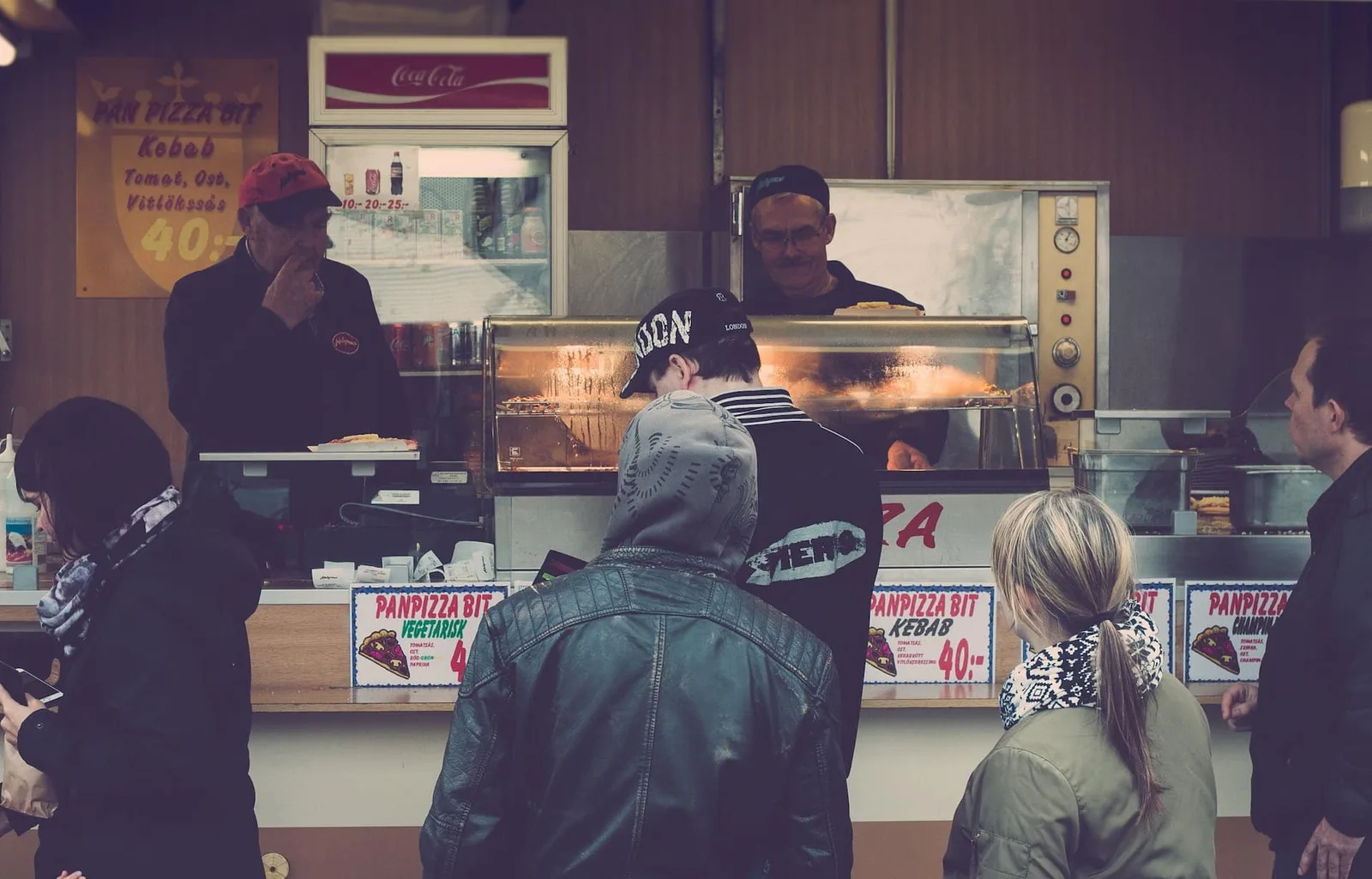 Foodtruck coloré stationné sur une place animée, avec un client commandant au comptoir et un panneau affichant le menu du jour.