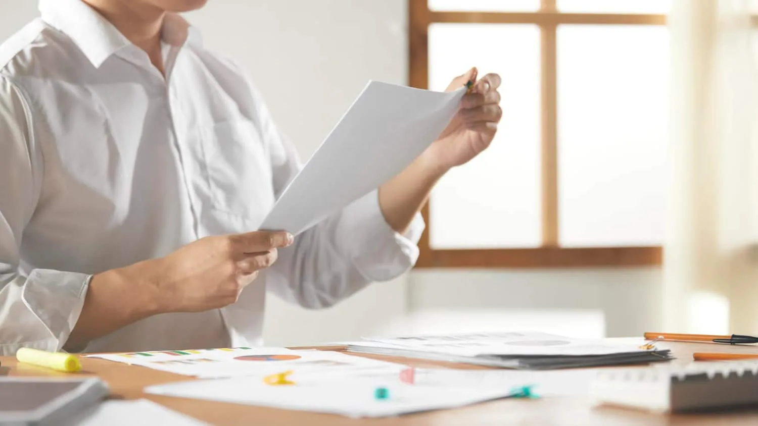 Deux collègues consultent un document sur un ordinateur portable avec un dossier de travail ouvert sur l’écran