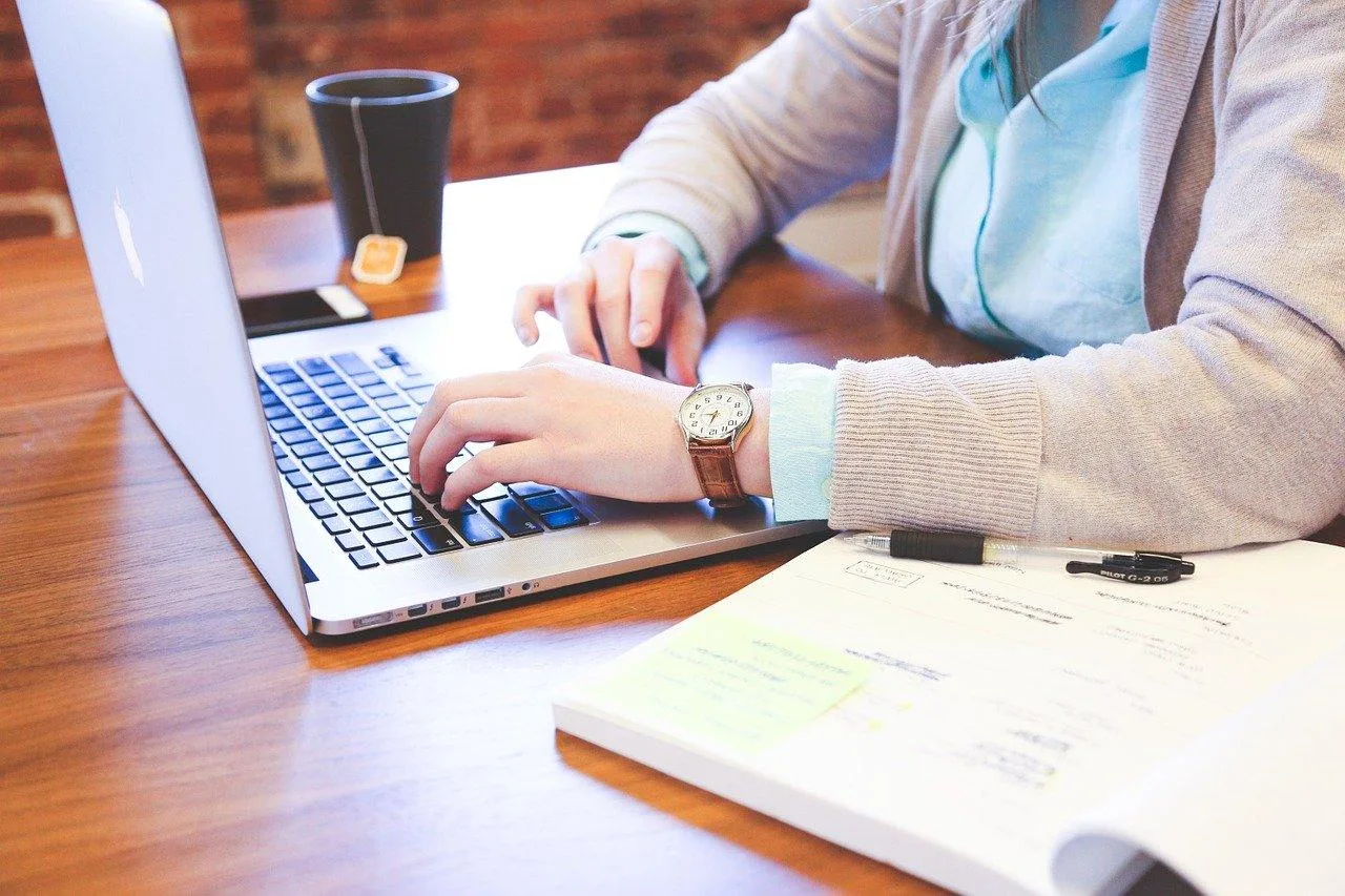 Entrepreneur individuel travaillant sur son ordinateur, avec carnet, téléphone et prototype de service sur un bureau.