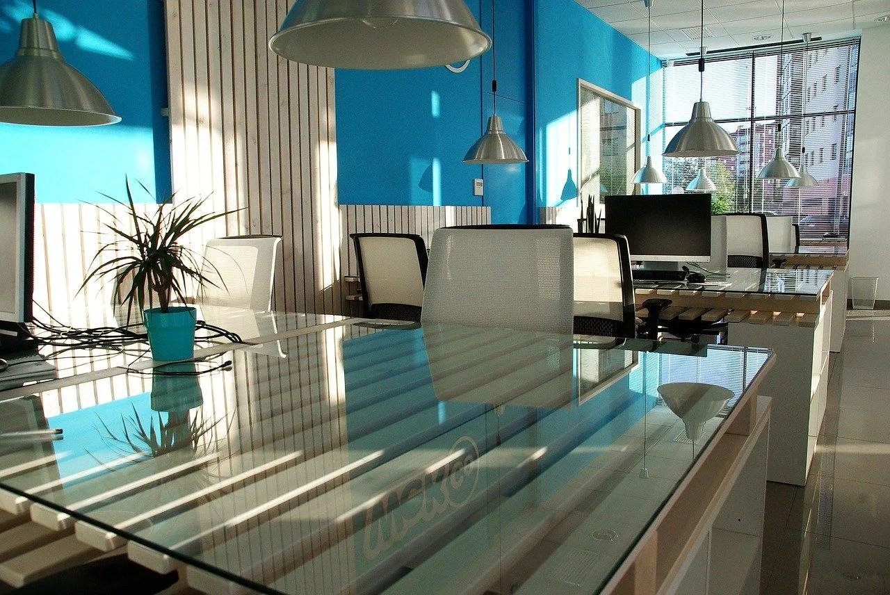 Freelance travaillant sur un ordinateur dans un espace de coworking lumineux avec tables partagées et salles vitrées