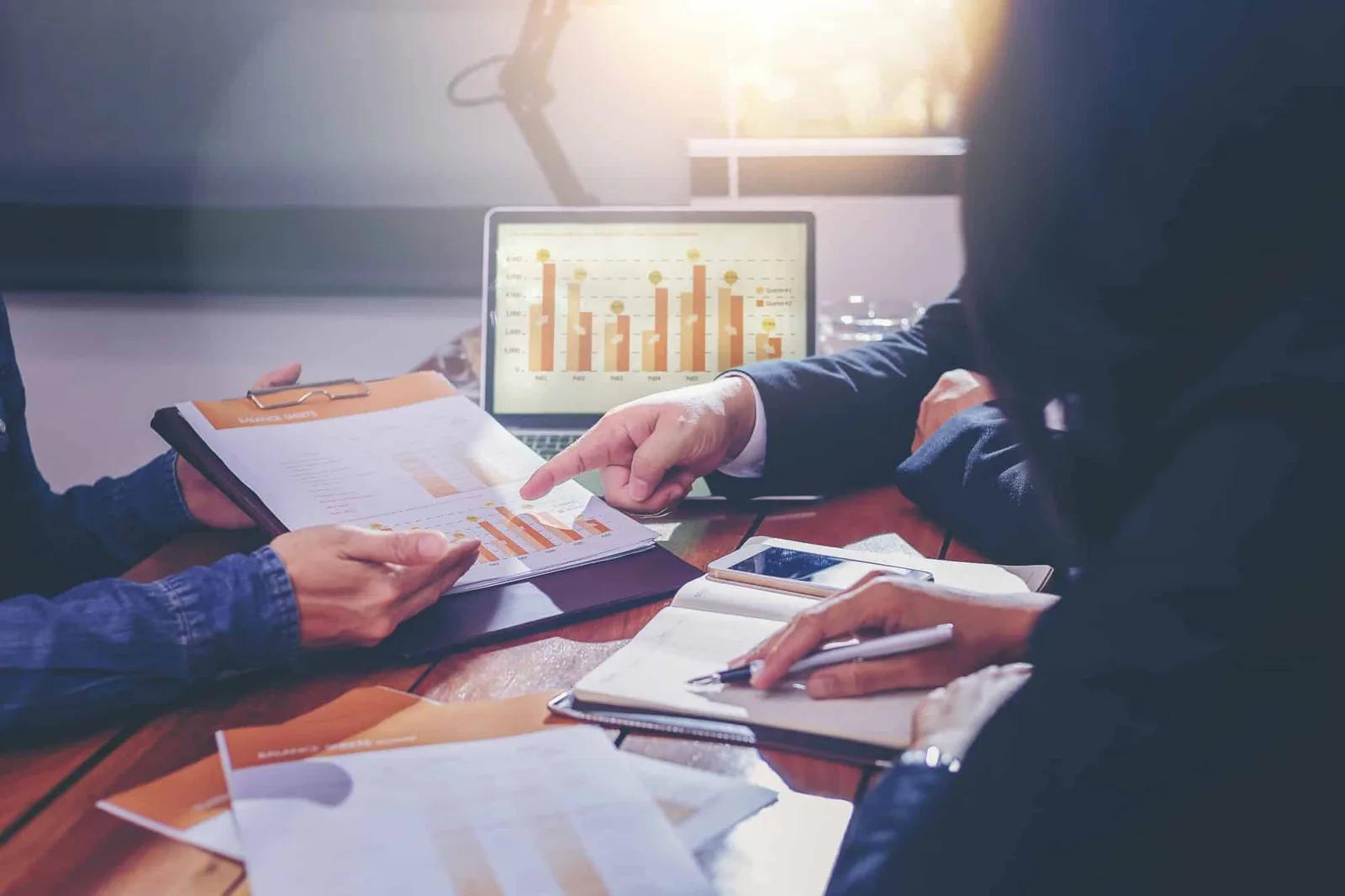 Entrepreneur individuel échange avec un expert-comptable autour d’un dossier de comptabilité et d’un ordinateur portable dans un bureau lumineux.