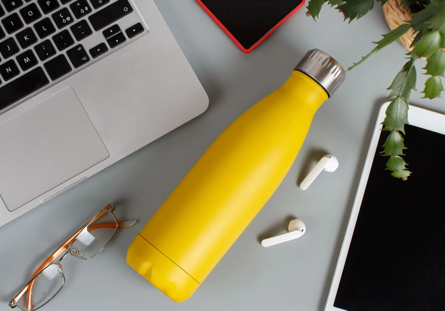 Une gourde réutilisable en inox avec un logo d’entreprise imprimé, posée sur un bureau à côté d’un carnet et d’un ordinateur portable.