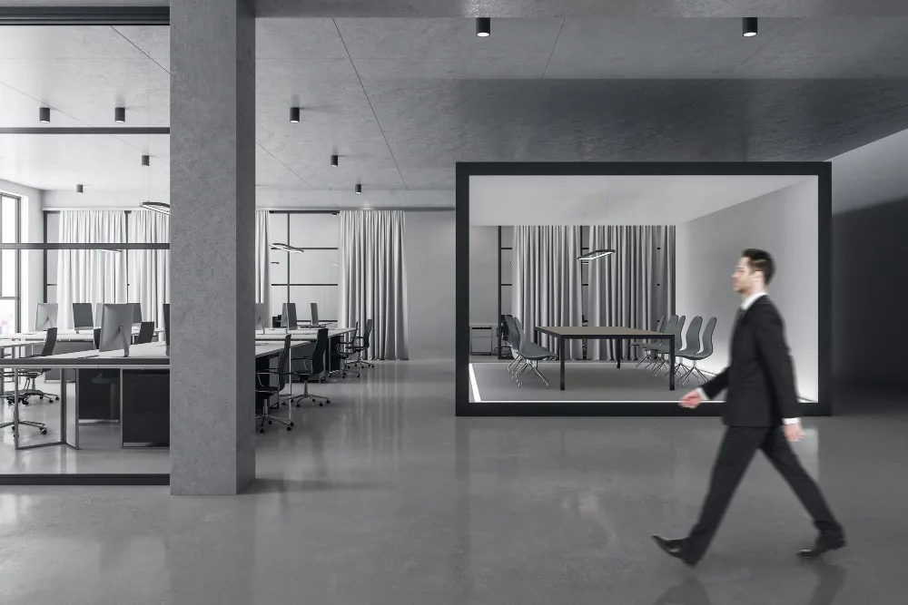 Un indépendant travaillant sur un ordinateur portable dans un espace de coworking moderne avec tables partagées et salles de réunion vitrées
