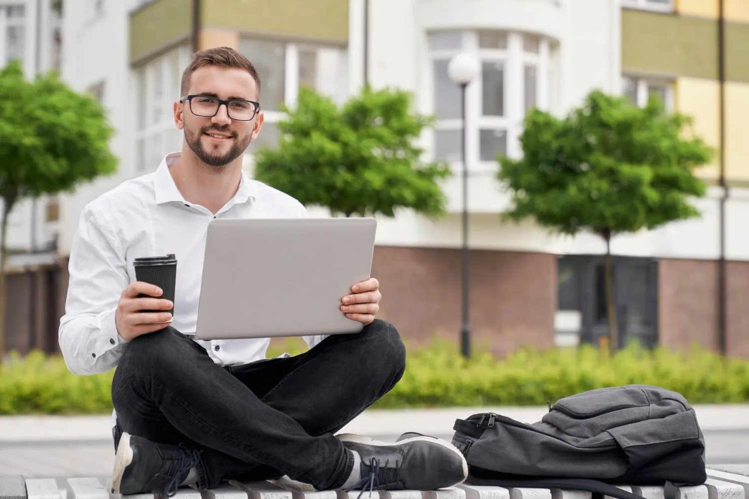 Un entrepreneur porte un sac à dos professionnel avec ordinateur portable, carnet et chargeur dans un environnement de travail moderne.