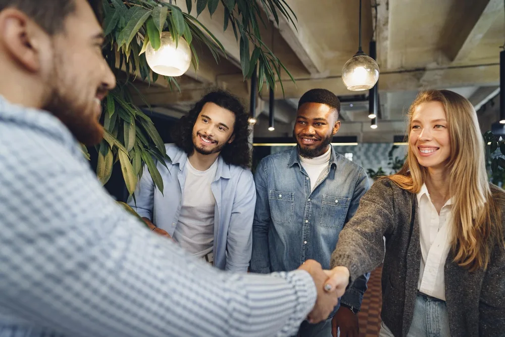 Deux entrepreneurs dans un espace de coworking échangent autour d’un prototype numérique et d’un tableau de projection financière.